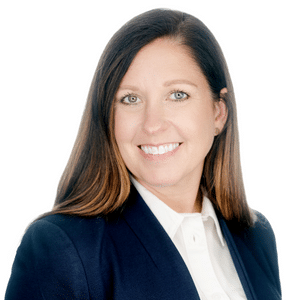 A professional woman in a navy blazer and white shirt smiles confidently at the camera, against a white background.