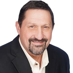 Man smiling in a suit jacket against a white background.