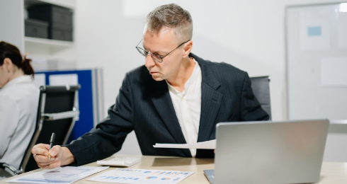 A man in a suit working at a desk with papers and a laptop.