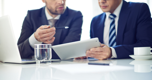 Two businessmen discussing work on a tablet in an office setting.