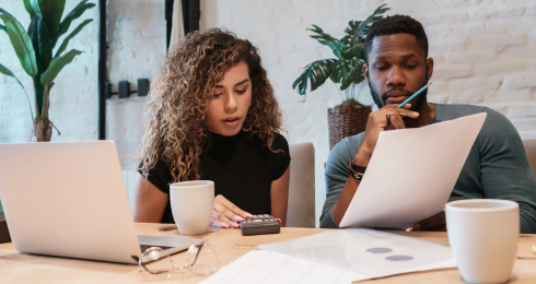 Two people collaborate in a modern office setting, reviewing documents with a laptop and coffee cups on the table.