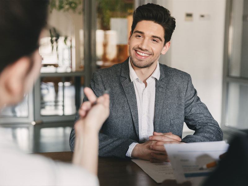 Man in a grey suit smiling during a business meeting in an office setting.
